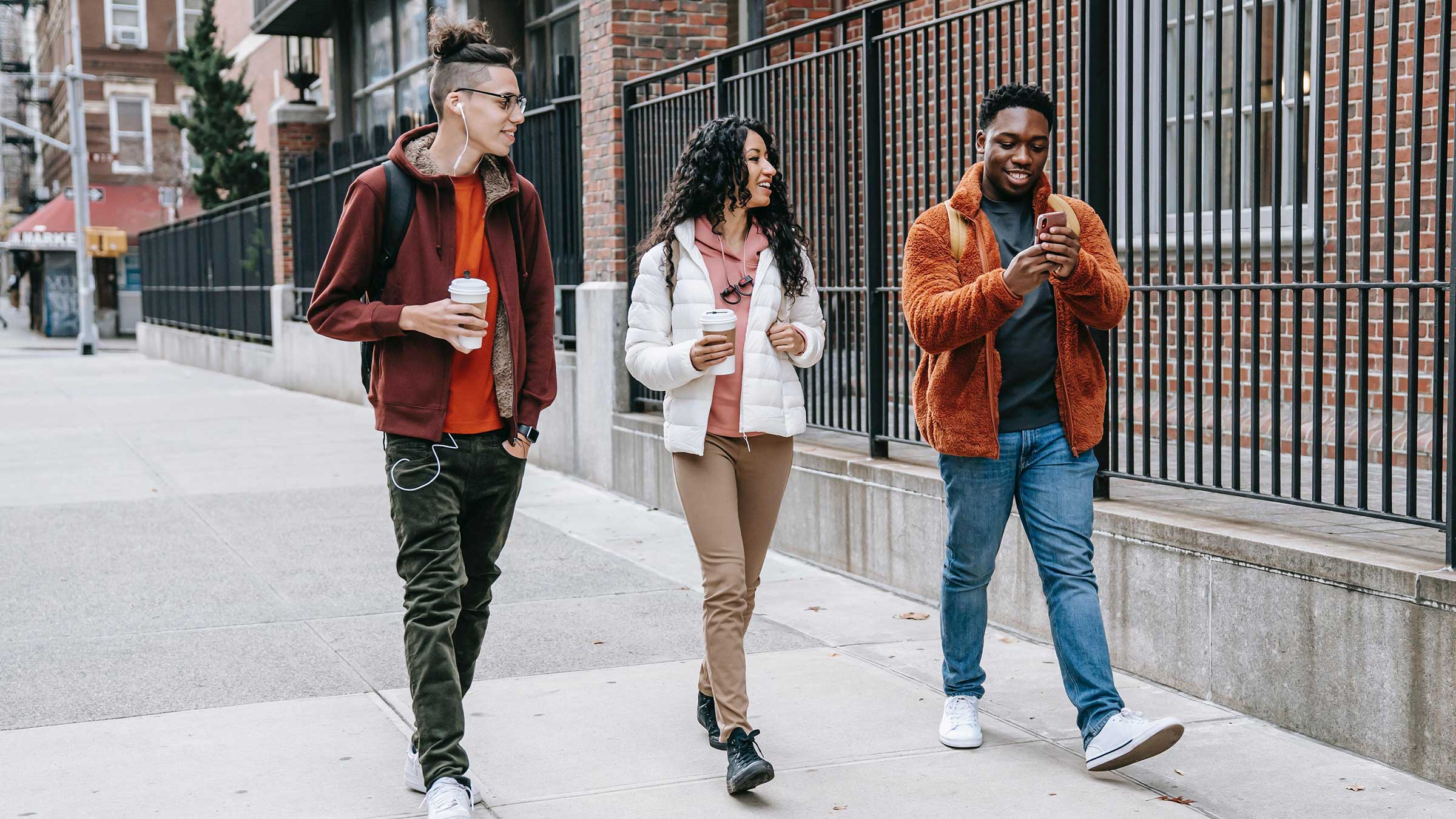 3 youths walking, 2 holding coffee cups and one looking at phone