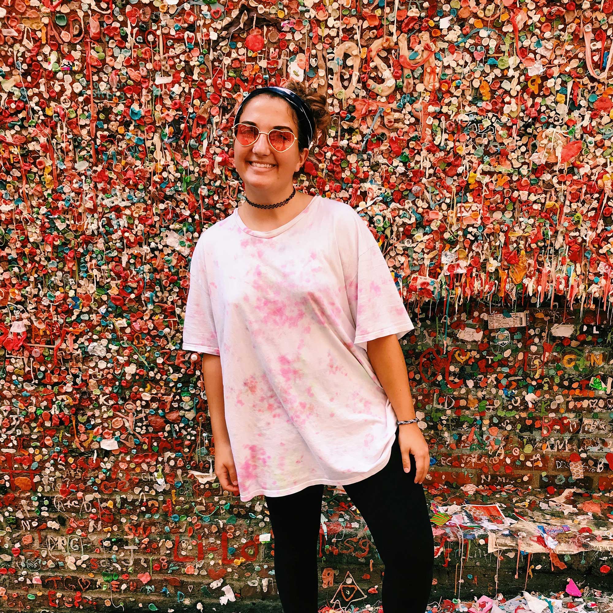 Savannah in sunglasses in front of a brick wall covered in colorful chewing gum
