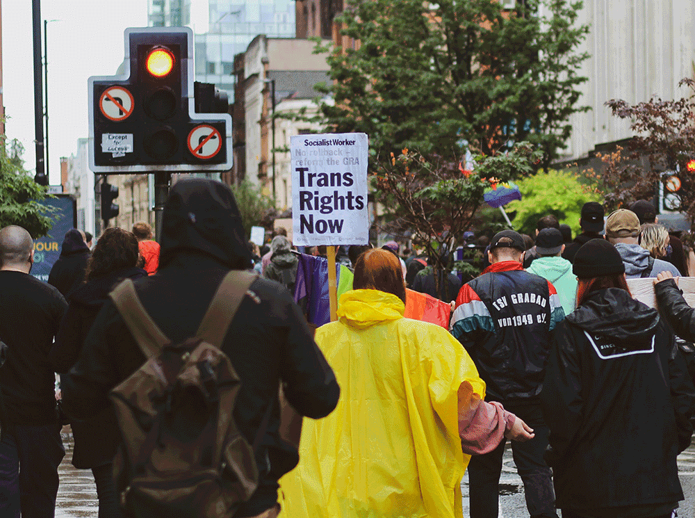 crowd of people walking with a sign that says Trans Rights Now