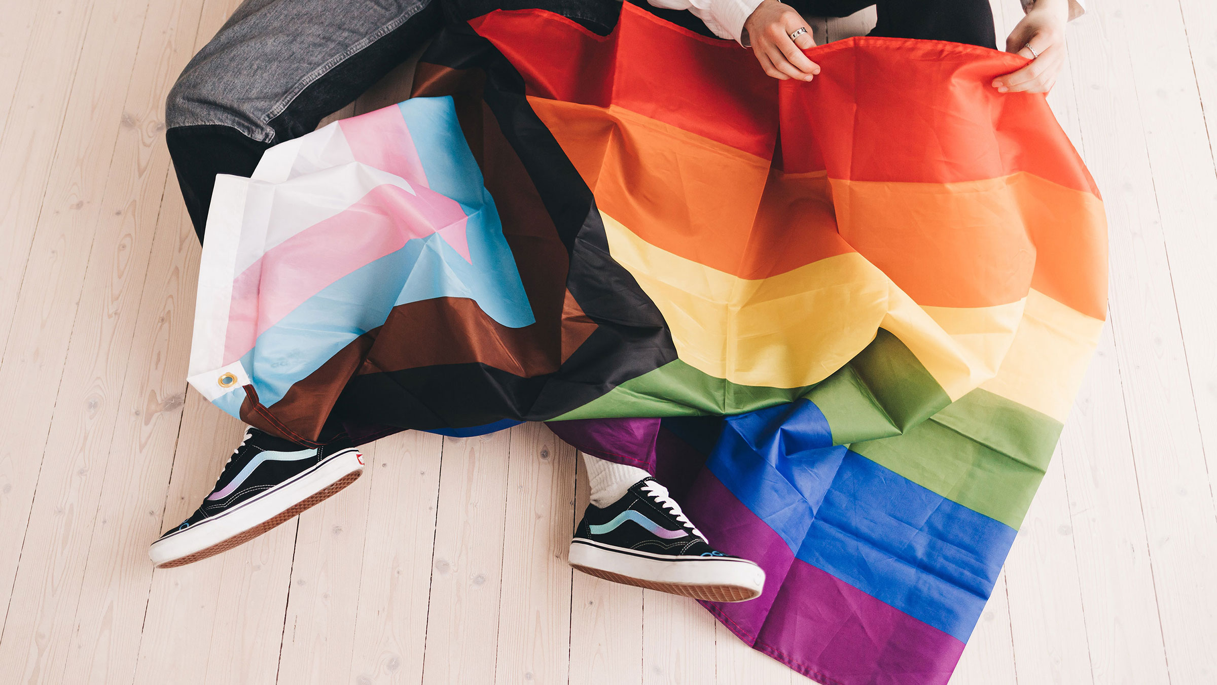 Progressive Pride flag lays over top of two pairs of legs