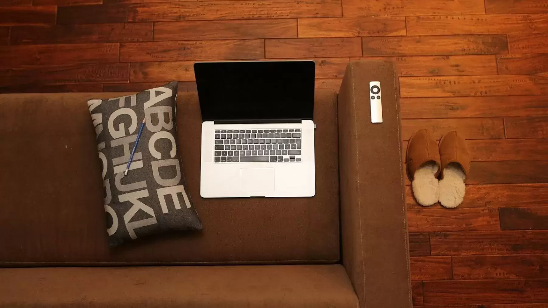 A laptop on top of a brown sofa with shoes nearby.