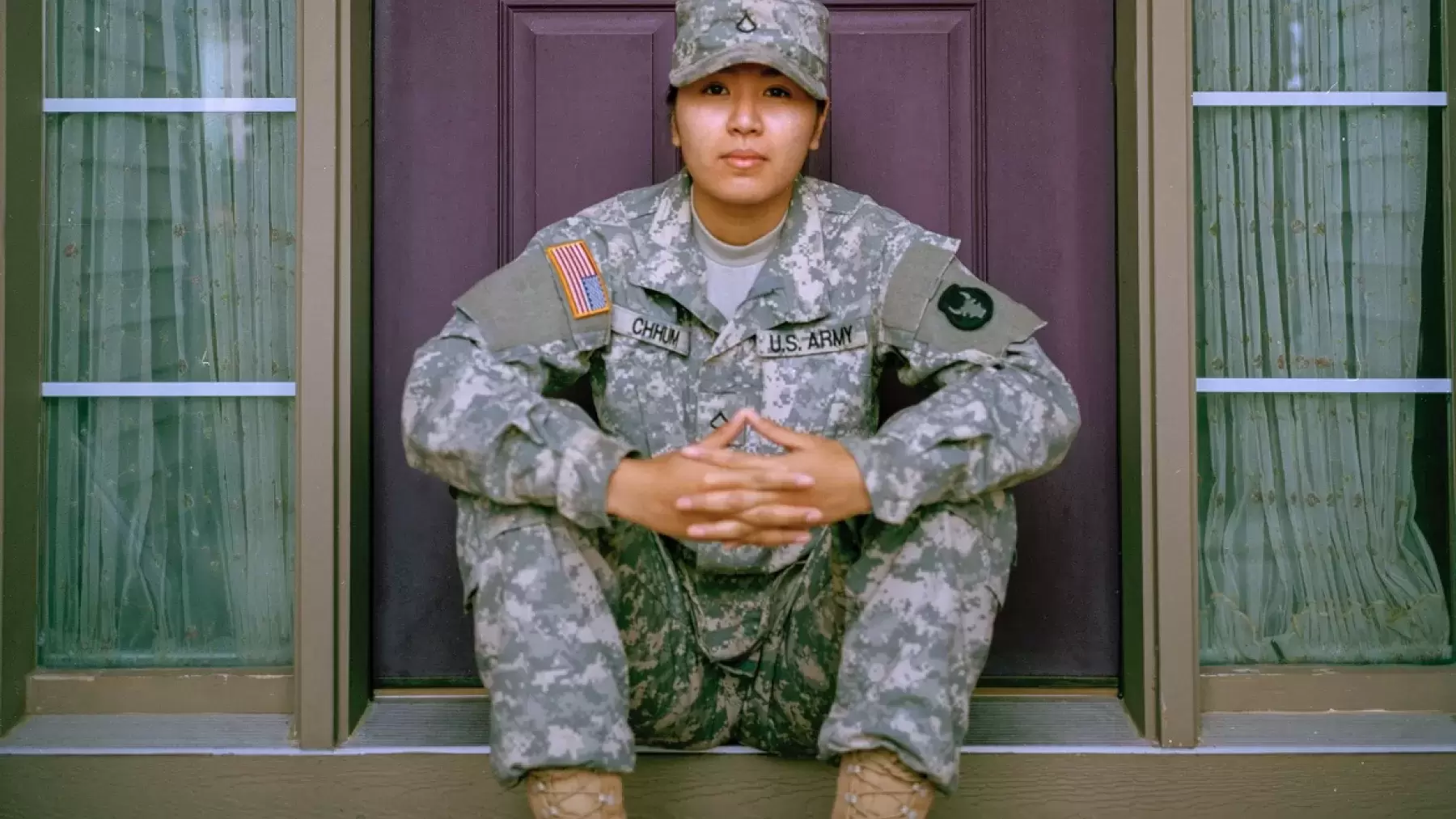 A feminine presenting soldier sitting on a porch in front of a purple door.
