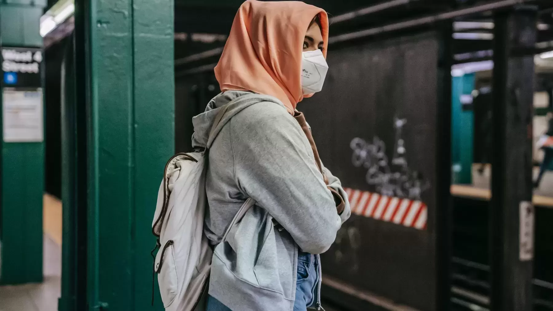 Woman in pink hijab and face mask looking over subway rails