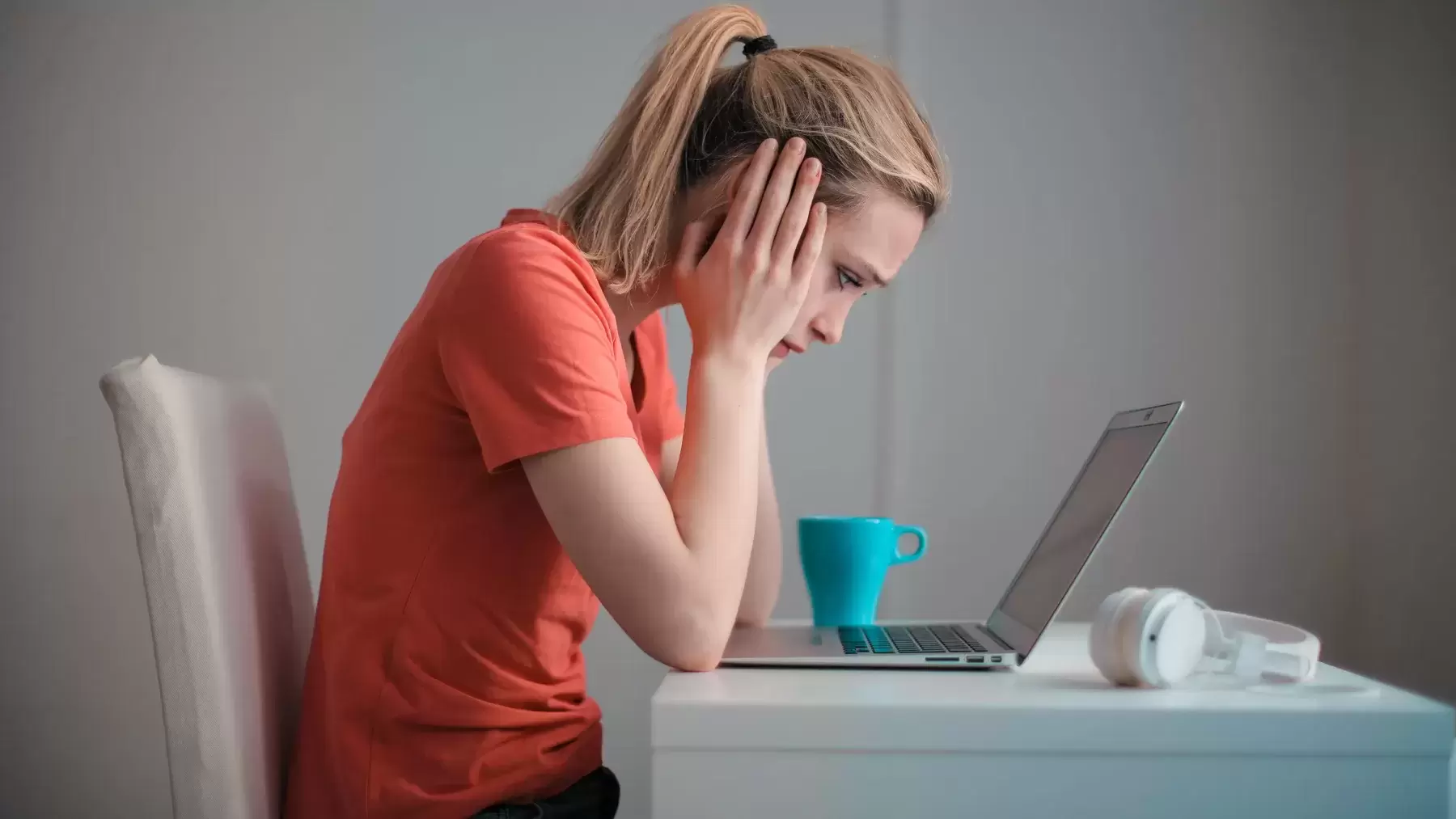 a woman hunches over her computer reading tough news with her hands on the side of her face