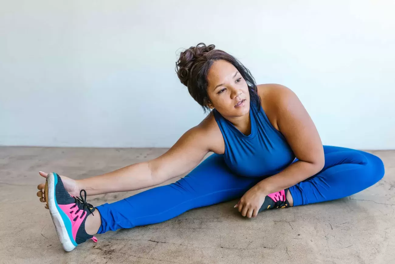 person in blue workout gear sits on floor and stretches, touching toes
