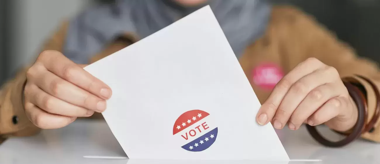 person holds white paper with Vote while putting it into a box