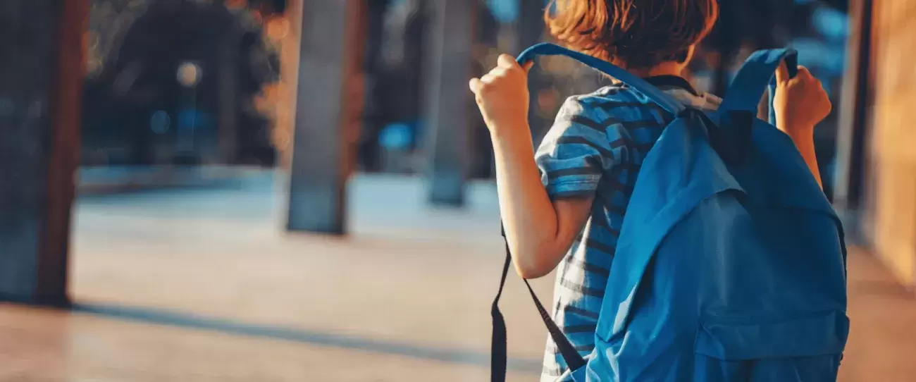 child stands with blue backpack on