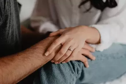 person with ring on finger holds the hand of someone else on their lap
