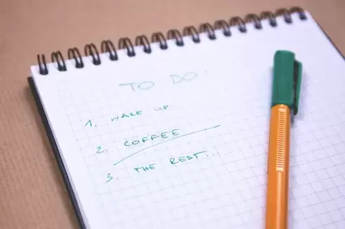 green and yellow pen rests on a notepad with graph paper and a to-do list with 3 items: 1. wake up, 2. coffee - underlined, 3. the rest...