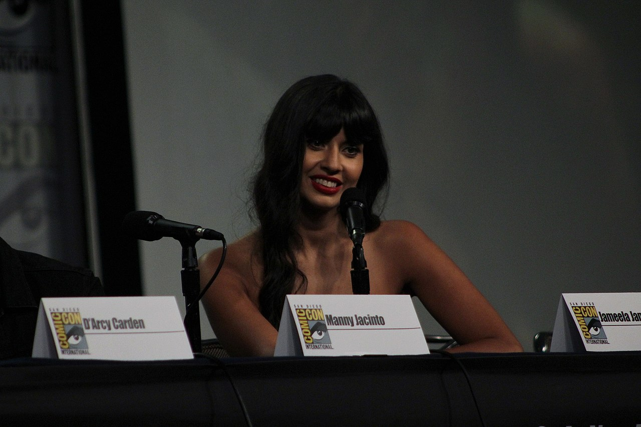 Jameela Jamil is seated at a microphone