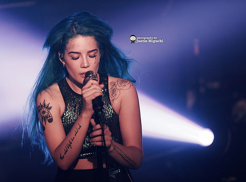 Halsey sings into a microphone with a spotlight shining behind her